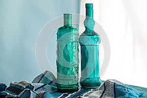 Still life with two hand crafted blue glass wine bottles made of recycled Spanish glass in front of window - horizontal image with