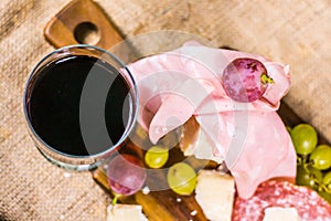 Still life - upper shot of yellow and red muscat grape, cheese, salami and a glass of red wine on a wooden board and canvas