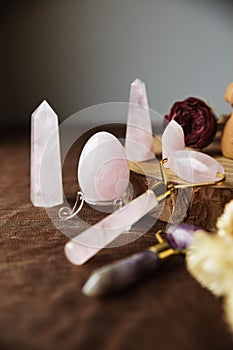 Still life with various rose quartz crystals and dried flowers egg, rose quartz face roller, and various obelisk-shaped stones