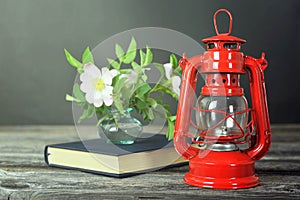 Still life with vintage oil lamp, book and dog rose flowers in vase on wooden background