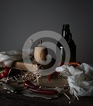 Still life, vintage. old bottle with oil, red pepper, mill, and a towel on wooden table.
