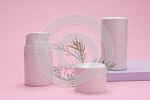 Still life with white blank bottles with moisturizer and herbal leaf on isolated pink backdrop. Mockup jars. Copy space