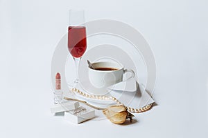 A still life with a white ceramic cup of coffee, a faded rose, a coral necklace, a lipstick, a box with the silver