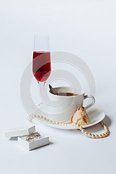 A still life with a white ceramic cup of coffee, a rose bud, a coral necklace, a little white box with the silver
