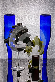 Still life with wine in glasses, grapes and inverted blue bottles
