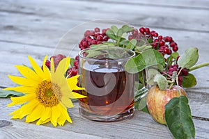 Still life on a wooden background. Black tea in a glass cup, sunflower flower, apples and rowan branch, top view