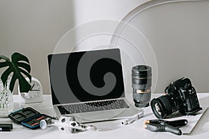 Still life working from home desk with professional photographic equipment, camera, lens, computer monitor, electronics indoors