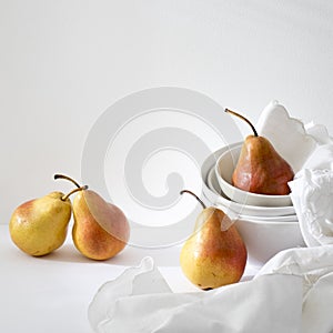 Still life with yellow-red pear Duchess in pile of bowls and a white embroidered napkin