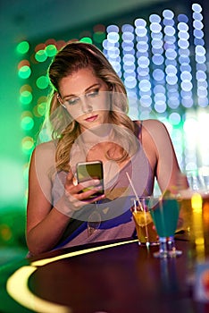 Still waiting.... Shot of young woman using her cellphone while sitting alone in a nightclub.