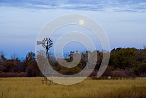 Still windmill standing in a brown grassy field backlit by the moon