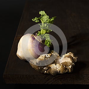Stillife of a turnip and an oyster mushroom on a wooden table against a dark background