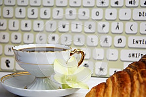 Stilllife of coffee cup with espresso, croissant or biscuit, flower and imitation of keyboard on a wooden background