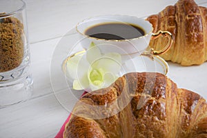 Stilllife of coffee cup with espresso, croissants, biscuits, tender flower, brown sugar on a wooden background