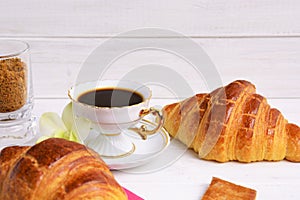Stilllife of coffee cup with espresso, croissants, biscuits, tender flower, brown sugar on a wooden background
