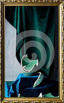 Stilllife with remnants of broken teal colored vase, emerald green and dark blue velvet, and picture frame photo