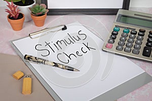Stimulus Check handwritten on a white sheet of paper on clip board with calculator pen office work space