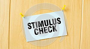 STIMULUS CHECK sign written on sticky note pinned on wooden wall
