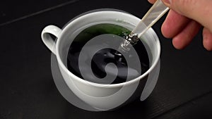 Stir chlorophyll extract in water in a white cup on a black cardboard surface.