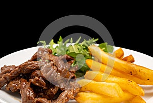 Stir-fried beef served with french fries and arugula leaves on white plate, isolated on black background. Close up view