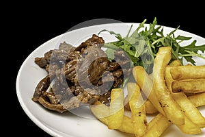 Stir-fried beef served with french fries and arugula leaves on white plate, isolated on black background. Close up view