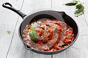 Stir-fried chicken breast in a sauce of tomatoes, garlic, basil and olive oil. Black cast-iron pan, light wooden table