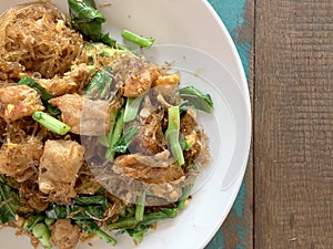 Stir fried Flat Rice Noodle with Soy Sauce and Pork in white dish on colourful wooden table in thai called `Pad See Eww`. Thai s