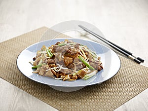 Stir-fried Hor Fun with Sliced Beef with chopsticks served in a dish isolated on mat side view on grey background