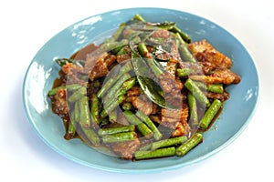 Stir fried pork belly and red curry paste with string bean in blue plate on white background.