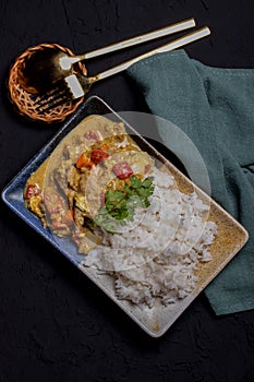 Stir fried pork curry powder with steamed rice in a plate on a black background