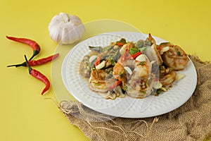 Stir-fried shrimp with chilli with garlic and chilli and spoon and fork with yellow background