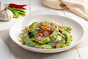 Stir fried snow peas with minced pork in white plate.