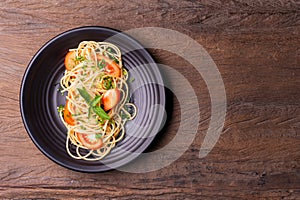 Stir-fried spaghetti or stir-fried noodles Tomato sauce and prawns on a black plate On a wooden table background. Top view