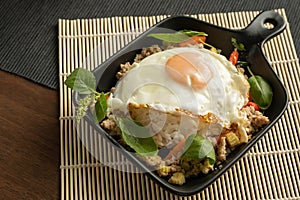 Stir-fried Thai basil with minced pork meat, carrots, and baby corns, with fried egg and fresh Thai basils sort in a black small