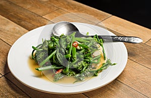 Stir Fried Water Spinach or Vietnamese fried morning glory, rau muong xao toi on white dish on wood table.