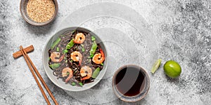 Stir fry buckwheat soba noodles with shrimps and vegetables in a bowl. Gray concrete grunge background. Asian