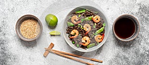 Stir fry buckwheat soba noodles with shrimps and vegetables in a bowl. Gray concrete grunge background. Asian traditional food.