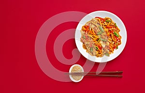Stir fry noodles with vegetables. Asian vegan food over red background, flat lay and copy space.