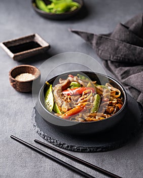 Stir-fry with soba noodles, meat and vegetables on dark background with napkin. Asian fast and healthy food concept