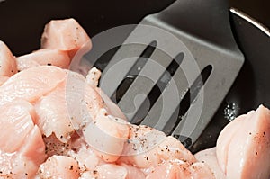Stir in raw chopped chicken breast with spices and salt in a frying pan. Plastic kitchen spatula