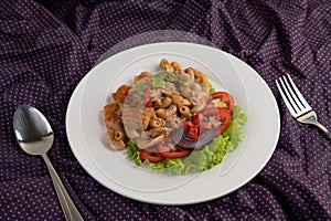 Stir shrimp macaroni on a white plate with fork, spoon, tomatoes and salad