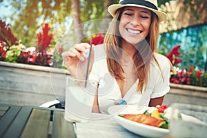 Stirred not shaken. a cheerful young woman wearing a hat and enjoying a cold beverage while being seated at a restaurant