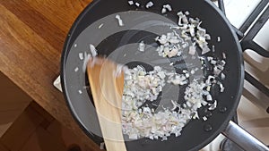 Stirring finely chopped onions in the home kitchen. Diced onions in a frying pan. Small chopped onions stirred with a