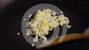Stirring fried sliced onion in hot frying pan by wooden turner. Close up