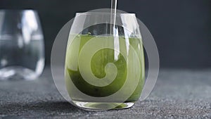 Stirring green barley grass powder in a glass of water - preparation of a healthy drink