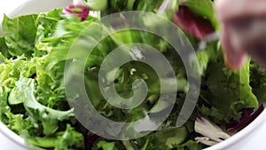 Stirring green lettuce in a white bowl.