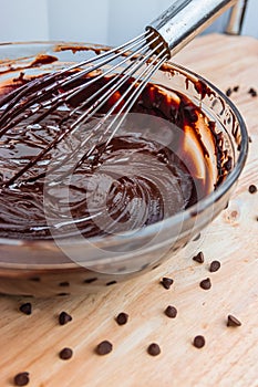 Stirring melted chocolate chips in bowl with whisk up-close on wood table