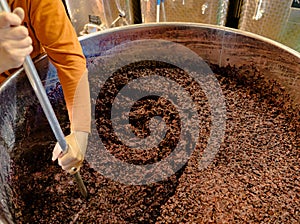 Stirring and mixing barrique pinot noir grapes fermenting in an open tank during wine-making