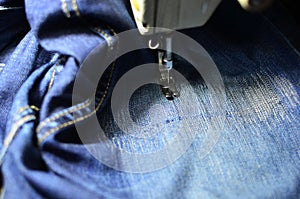 Stitching, stitching a hole in blue jeans with a sewing machine. Part of sewing machine and jeans cloth closeup.