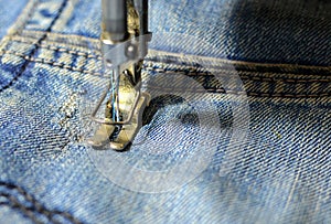 Stitching, stitching a hole in jeans with a sewing machine. Part of sewing machine and jeans cloth closeup. Tailoring