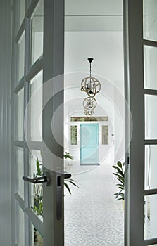 Stylish and light hall interior design with white walls and floor, blue doors, plants and pictures.